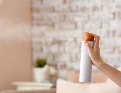 Person holding an air freshener spray can in a home setting, illustrating indoor air quality management and the reduction of volatile organic compounds (VOCs).